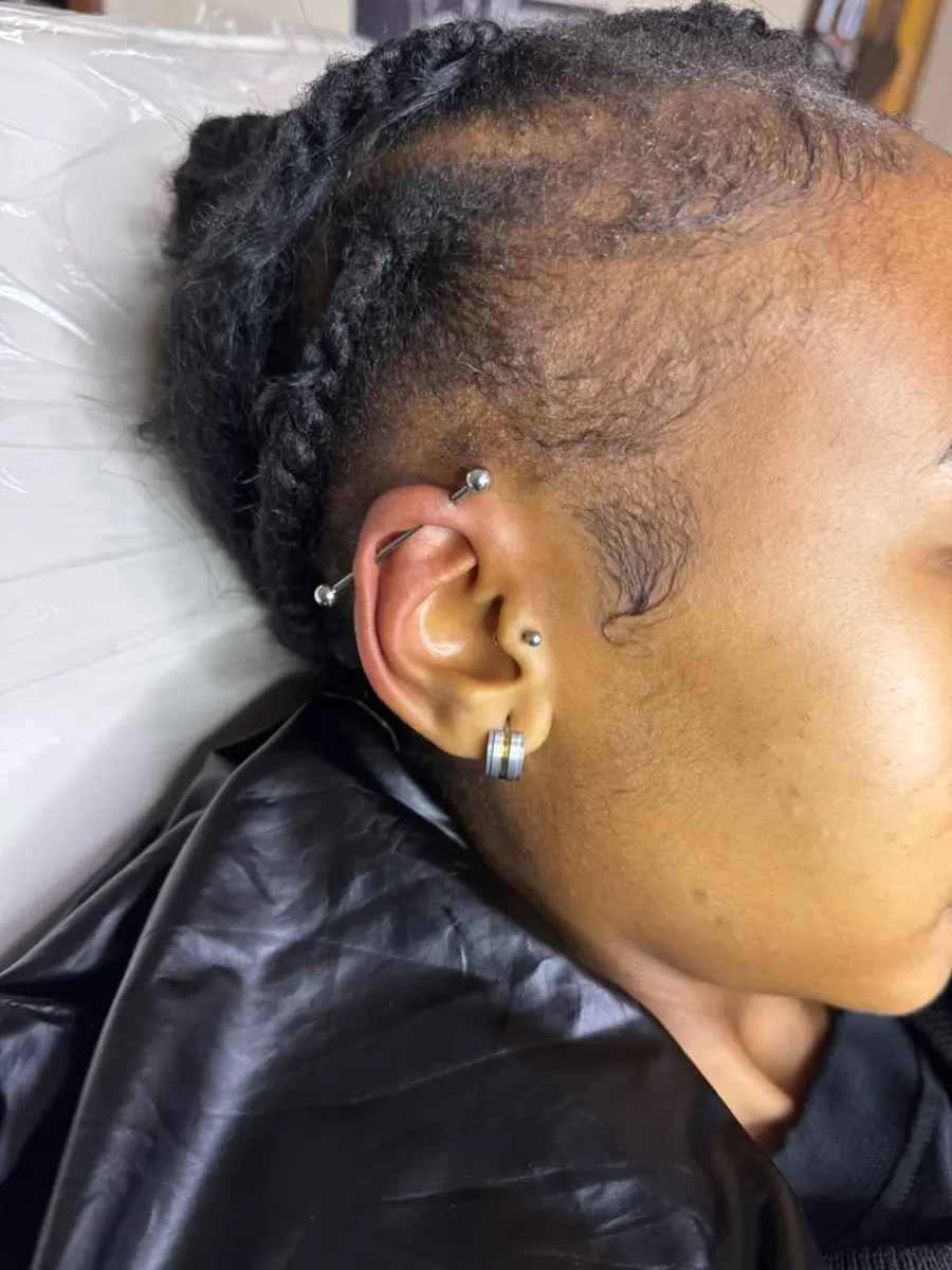 Close-up side view of a person's ear and braided hair, showing multiple ear piercings and earrings
