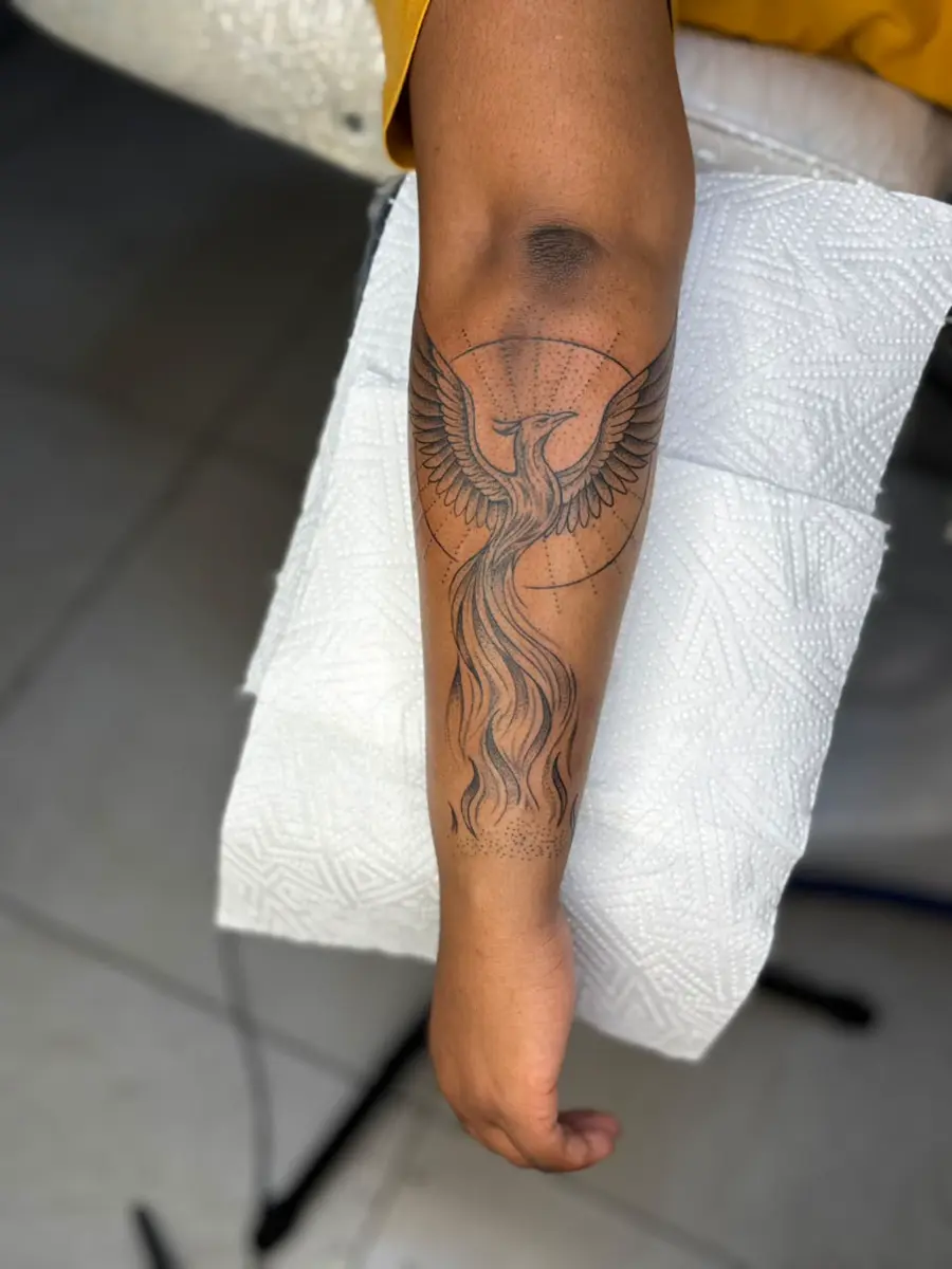 Forearm with a large phoenix tattoo resting on a white textured paper towel