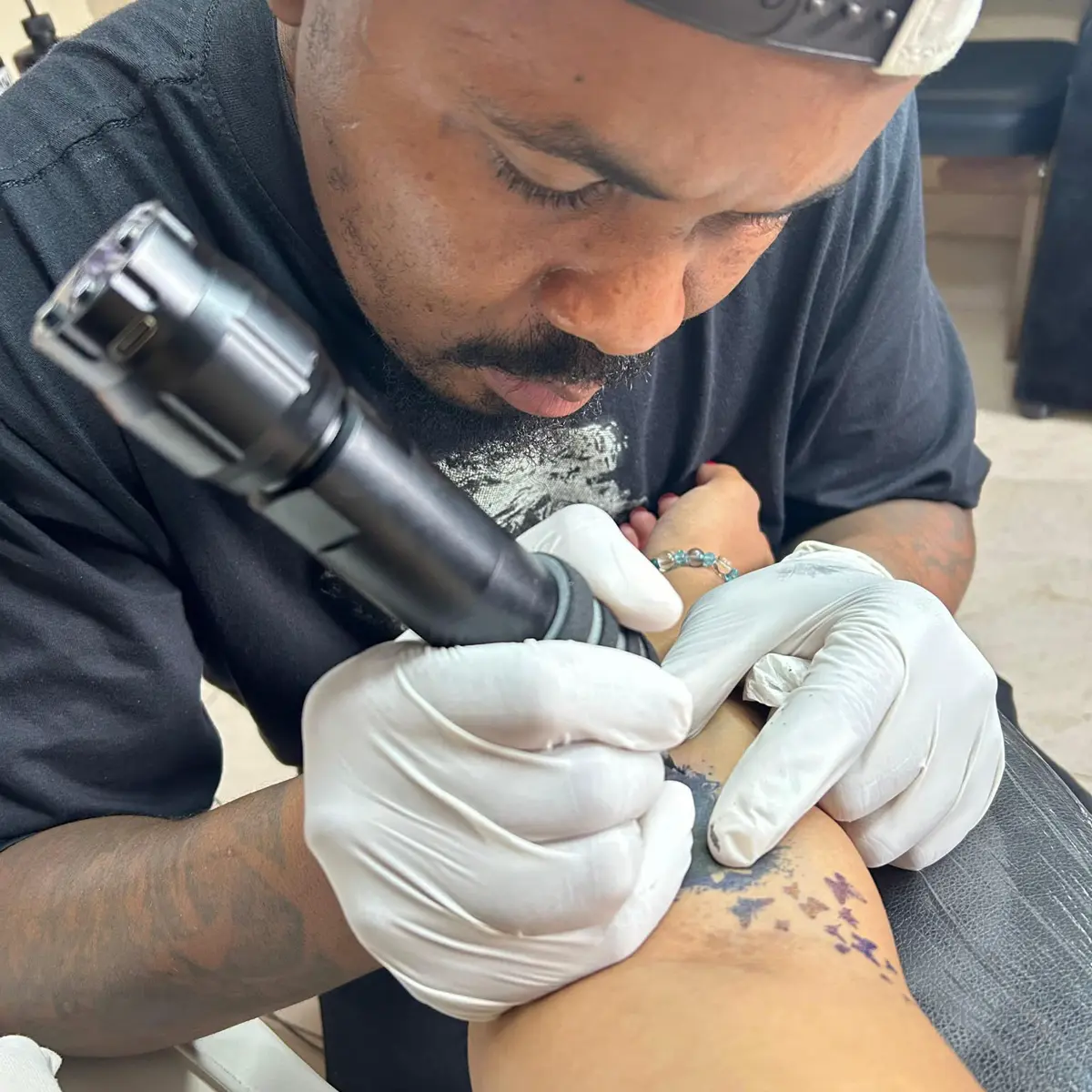 Tattoo artist wearing white gloves using a tattoo machine on a client's arm