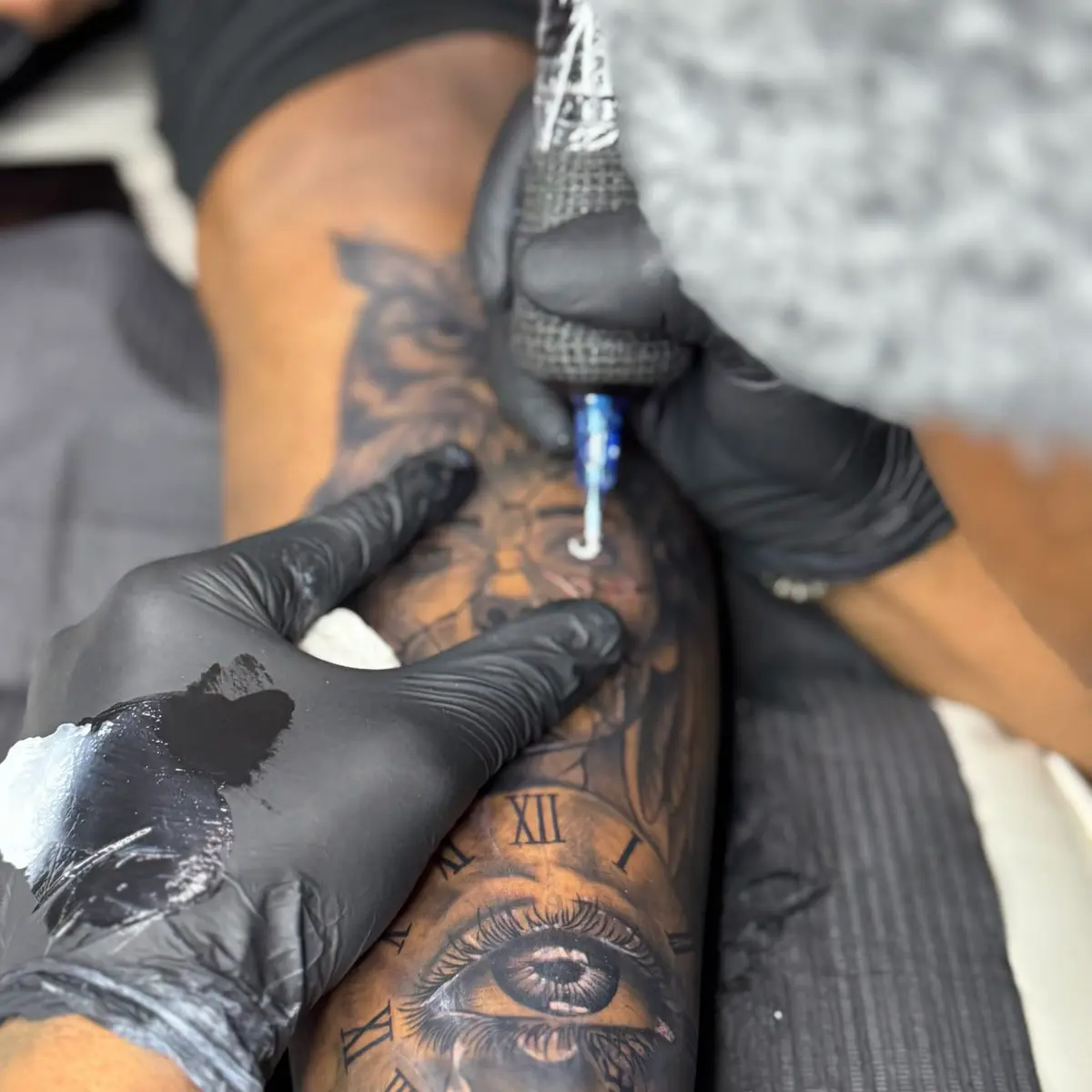 Tattoo artist in black gloves working on a heavily tattooed forearm